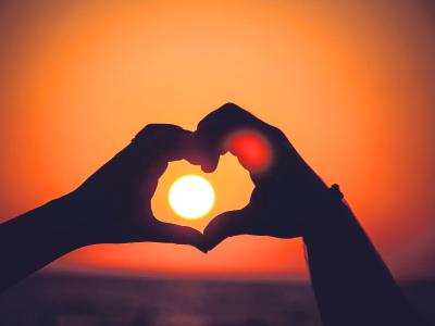 Mani formano un cuore con il sole al tramonto.