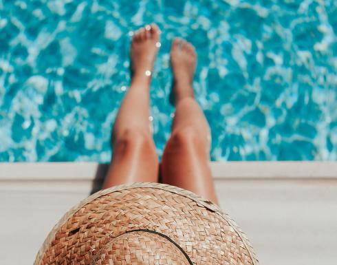 Persona che si rilassa vicino alla piscina con un cappello di paglia.