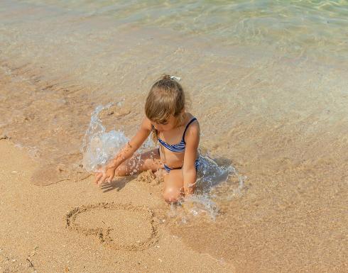 Bambina gioca sulla spiaggia disegnando nella sabbia.