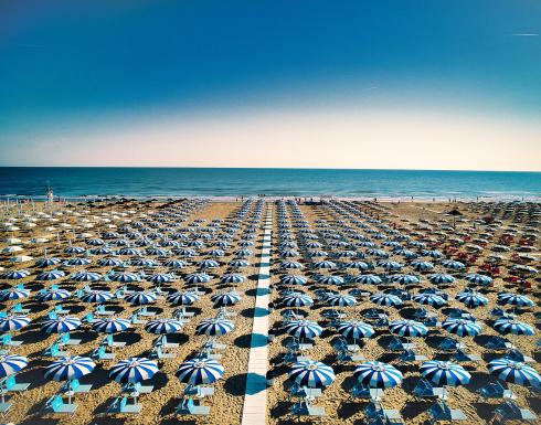 Spiaggia con ombrelloni blu e bianchi allineati, vista mare.
