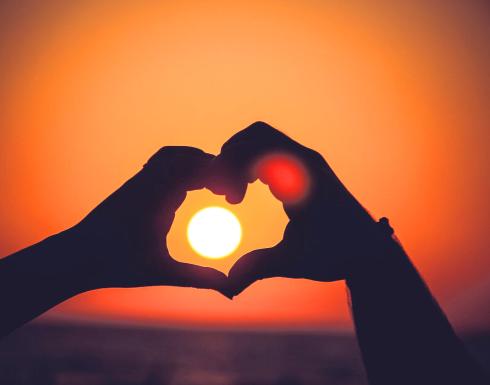 Mani formano un cuore con il sole al tramonto.