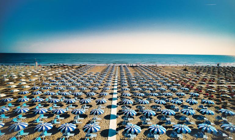 Spiaggia con ombrelloni blu e bianchi allineati, vista mare.