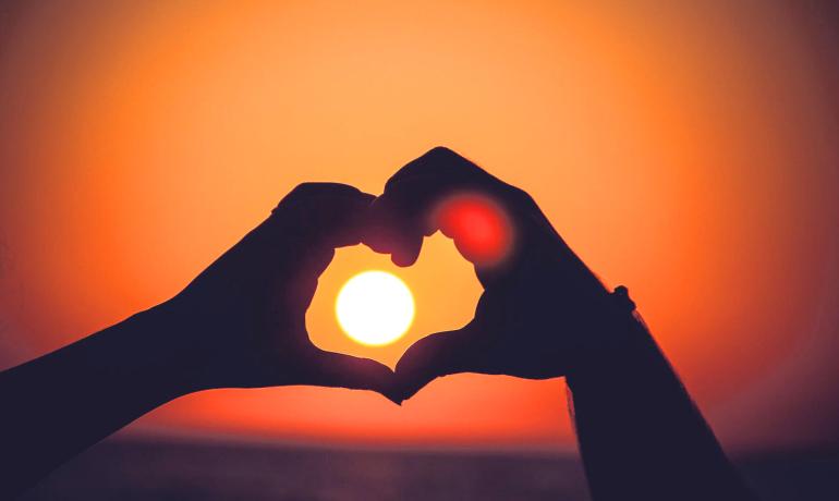 Mani formano un cuore con il sole al tramonto.