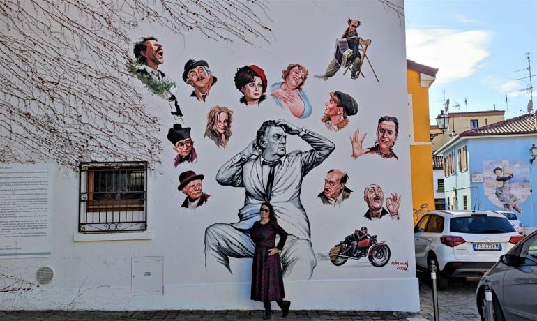 Buntes Wandbild mit berühmten Gesichtern und einer Person, die davor posiert.