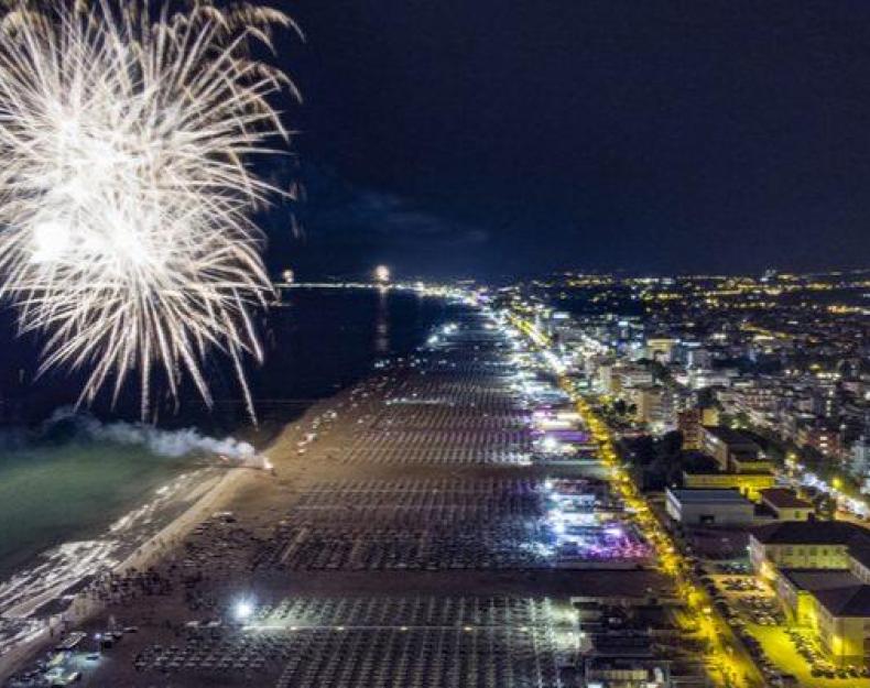 Feux d'artifice illuminent la plage la nuit, vue panoramique de la ville côtière.
