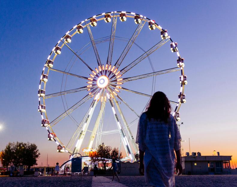 Donna davanti a una ruota panoramica illuminata al tramonto.